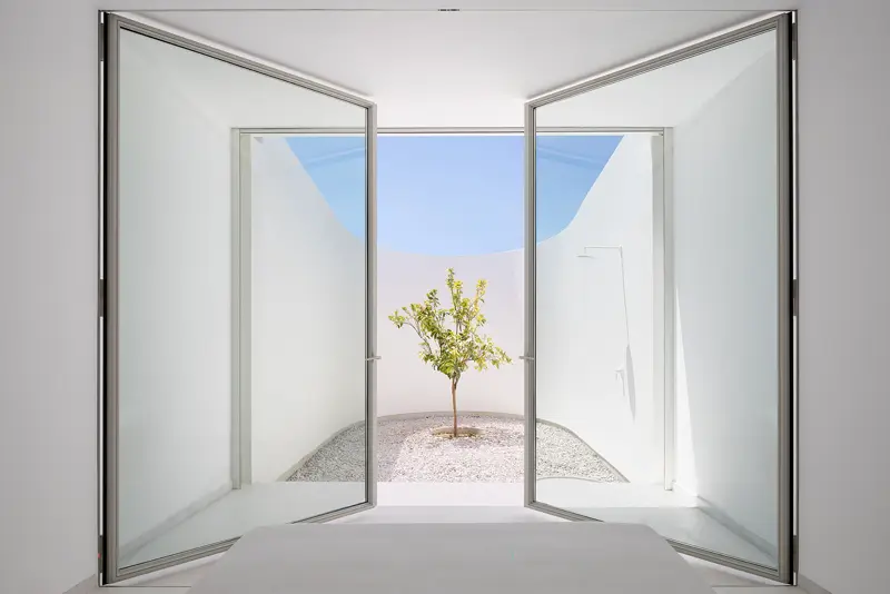Puertas pivotantes de acero abiertas hacia un patio con un árbol