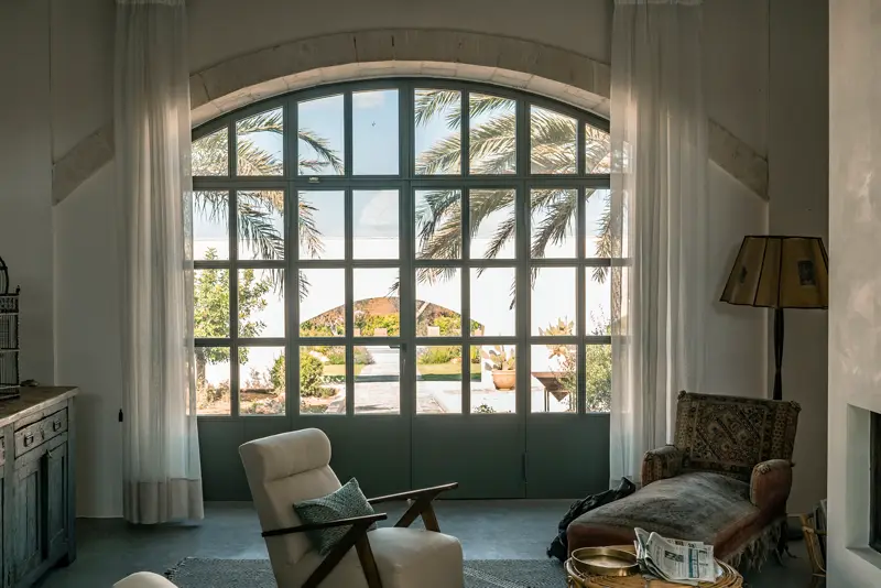 Ventana de acero en arco con vista a un patio con palmeras